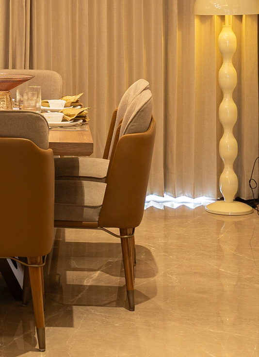 Contemporary Casa Homes dining room with a long rectangular table, beige cushioned seating, and ambient wall lighting enhancing the cozy, refined atmosphere.